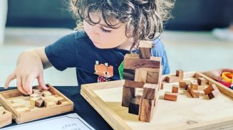 Young child playing with wooden puzzle blocks at a table, concentrating on building and arranging pieces on a wooden board.